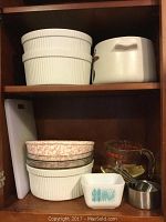 Photo showing vintage mixing bowls, cutting board, Pyrex measuring cup, and metal measuring cups on cabinet shelf.