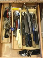 Top view of an open drawer containing organized kitchen utensils including knives, spoons, corkscrews, and an electric hand mixer.