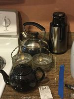 Overall view of the lot showing the stainless steel kettle, black ceramic teapot, coffee server, glass sugar bowls in metal caddy with spoons.