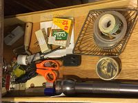 Assorted hardware, light bulbs, scissors, pencils, sinew, glue, knife, and electrical items arranged on a wooden surface.