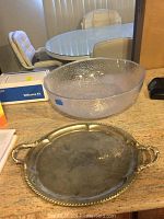 Clear textured plastic salad bowl and oval silver plated serving tray with handles on a table.