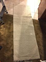 Beige entryway rug with raised square pattern shown rolled out on carpeted floor.