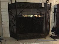 Photo of the wrought iron fireplace screen with palm tree design in front of a white brick fireplace.