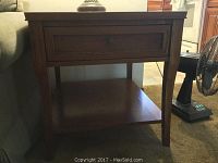 Full view of oak side coffee table showing front drawer and lower shelf against a couch and kitchen background.