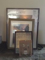 Photo showing six framed pieces, including the largest new frame still in plastic packaging behind smaller framed art and calendar pieces.