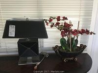 Side view of lamp and faux orchid on curved wooden surface with blinds background