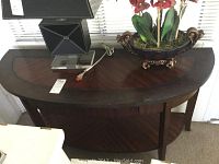 Front and top view of wooden semi-circular entry way table showing inlay design, single drawer, and bottom shelf.