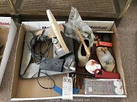 Various tabletop items including a decorative light fixture, incense holders, candles, lighter, and electrical accessories arranged in a cardboard box showing wear and used condition.