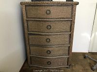 Front view of the wicker chest showing five drawers with metal ring pulls and bun feet.