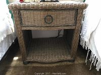 Front view of wicker side table showing drawer with metal ring pull and open shelf below.