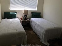 Two twin beds side by side with white coverlets and green pillows, nightstand and lamp between