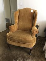 Front view of gold/mustard wing chair showing upholstery texture, shape, and wooden legs.