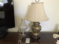 Glass oil lamp, brass figurine, and brass table lamp with shade on a wooden surface.