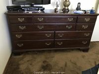 Frontal view of wood dresser showing ten drawers with brass pulls and dark brown finish on a carpeted floor.