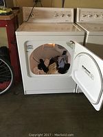 Front view of white Kenmore electric clothes dryer with door open showing clothes inside drum and interior light on.