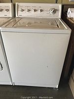 Front view of white Kenmore top-load washing machine with closed lid and visible control panel.