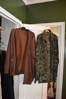Two men's coats hanging on hangers on a door, one brown zip-up coat, one green coat with southwestern pattern.