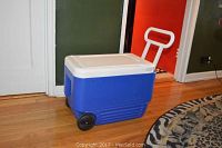 Blue and white Igloo wheeled cooler on wooden floor, closed lid shown.
