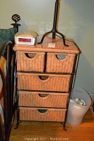 Black wrought iron side table with five woven drawers, placed next to a bed.