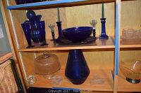 Shelf with cobalt pitcher and two tall cobalt glasses on left, candlesticks and bowl with tray center