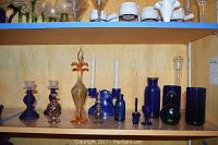 Shelf display of cobalt blue glass items including candlesticks, bottles, vases, candy bowl, and decorative perfume bottles.