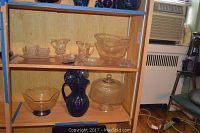 Shelf display showing the cobalt pitcher on middle shelf, clear glass bowls on top and bottom shelves, and a footed cake server with lid beside pitcher.