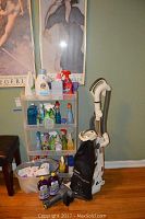 Photo showing Shark Navigator upright vacuum with attached hose and accessory attachments, Shark cordless vacuum nearby, and plastic shelving unit stocked with various cleaning supplies including sprays and detergents.