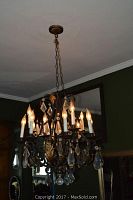 Chandelier illuminated, showing glowing candle-style bulbs and hanging crystal drops, suspended by an iron chain.