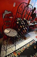 Photo showing the wrought iron chair with decorative face design and tiled seat next to the tall black wrought iron wine rack housing multiple wine bottles.
