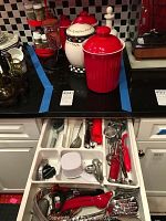 Photo shows four ceramic kitchen jars with lids in red, white, and decorative checkered designs on black countertop along with two clear spice racks filled with spice jars.