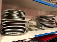 Stacks of white edged plates and bowls on shelves, some with decorative jungle pattern edges visible