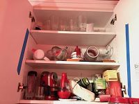 Wide shot of cabinet with multiple kitchen items including glassware, hand blender, tea boxes, and miscellaneous utensils.