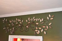 Front view of wrought iron and mirrored leaf branch wall hanging mounted above door frame on green wall.