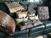 All pillows arranged on a black leather couch showing mix of animal print pillows and throw blanket