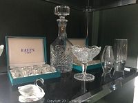 Wide view of shelf with large crystal decanter, crystal goblets, glass vases, Eales salt shakers in box, and Swarovski crystal swan.