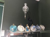 Six demitasse cup and saucer sets arranged on a shelf with a wrought iron candle lamp mounted above.