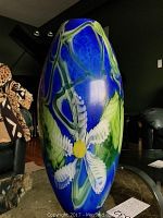 Front angle of the vase showing the blue hand-blown glass with white flower, yellow center, and green accents.