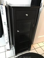 Black wooden cabinet with top drawer and lower shelf door, crystal-like knobs, minor surface scratches visible.