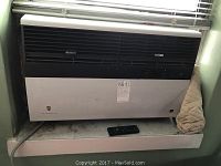 Front full view of the Friedrich window air conditioner installed in window with remote control on the ledge.