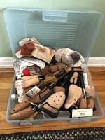 Plastic storage bin filled with assorted shoe care items including wooden shoe shapes, brushes, cloths, and polish bottles.