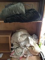 Stack of folded electric fleece blankets on top shelf and pile of handmade crocheted textiles below on wooden shelves.