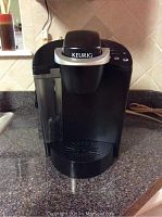Front view of black Keurig coffee maker on countertop showing water reservoir and drip tray