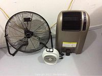 Patton 24-inch floor fan, white Warmwave heater, gold-toned Lasko space heater with remote control all placed side by side on floor.