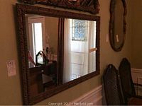 Full view of the mirror hanging on a wall reflecting furniture and window detail, showing the overall design and size.