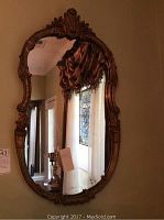 Full view of vintage oval mirror mounted on wall, showing carved gold floral frame with intricate design details.
