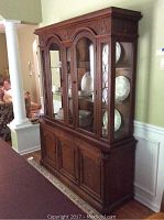 Angle view of dark wood china cabinet showing three glass doors on top and three wooden storage doors below, standing against a wall in a home interior.