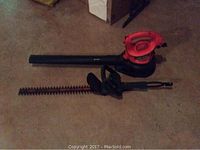 Black and Decker electric leaf blower with attached blower tube and hedge trimmer blade laid on floor, showing overall shape and condition.