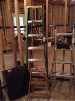 Photo of both ladders positioned upright in a basement alongside other items.
