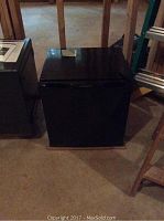 Closed mini refrigerator showing compact black exterior in basement setting.