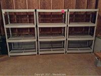 Front view of three plastic shelving units with four vented plastic shelves each, lined up against an unfinished basement wall.